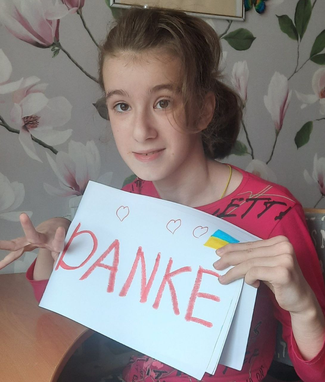 Ein Mädchen hält ein selbstgemaltes Blatt mit der Aufschrift „DANKE“, Herzen und einer ukrainischen Flagge in die Kamera.